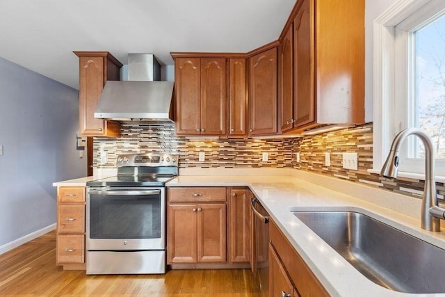 kitchen with wall chimney range hood, sink, light wood-type flooring, tasteful backsplash, and stainless steel appliances