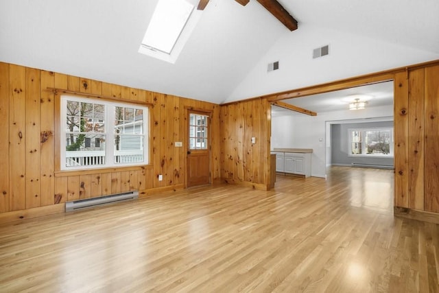 unfurnished living room featuring lofted ceiling with skylight, a baseboard radiator, wood walls, and light wood-type flooring