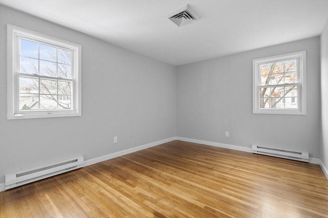 spare room featuring a healthy amount of sunlight, light wood-type flooring, and a baseboard heating unit