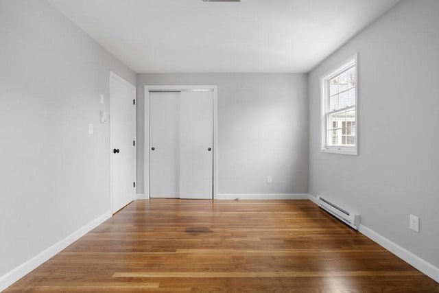 empty room with wood-type flooring and a baseboard heating unit