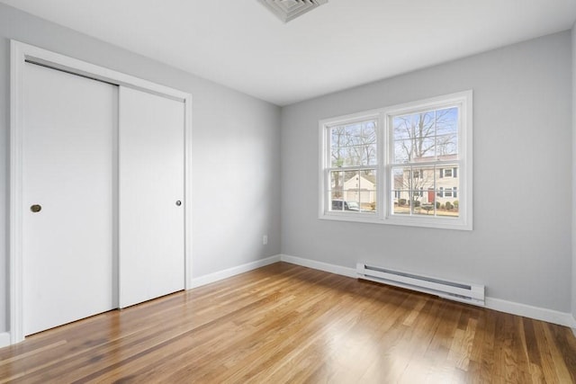 unfurnished bedroom featuring baseboard heating, a closet, and hardwood / wood-style flooring