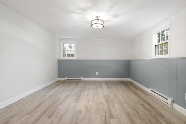 unfurnished room featuring light wood-type flooring, a wealth of natural light, and a baseboard heating unit