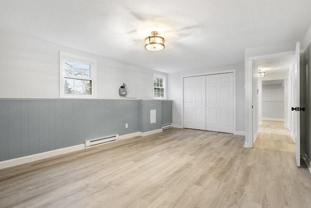 unfurnished bedroom with light wood-type flooring, multiple windows, and a baseboard heating unit