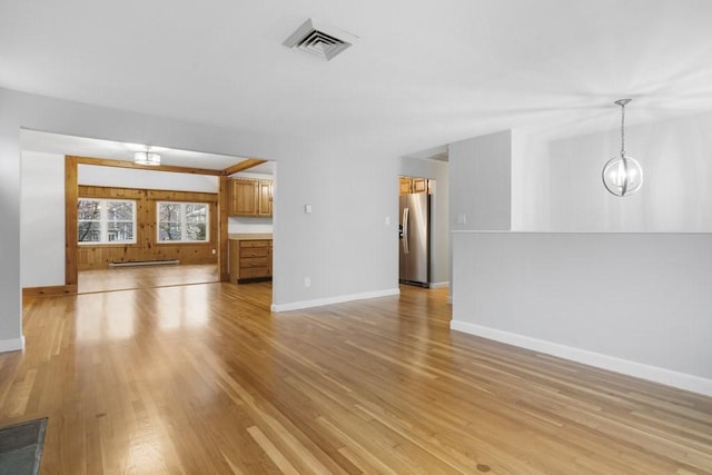 unfurnished living room featuring light hardwood / wood-style floors, baseboard heating, and an inviting chandelier