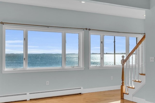 unfurnished room with a healthy amount of sunlight, a water view, light wood-type flooring, and a baseboard radiator