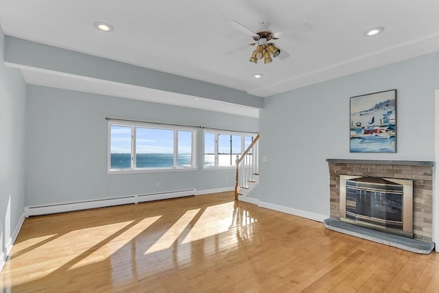 unfurnished living room with ceiling fan, a brick fireplace, a baseboard heating unit, a water view, and hardwood / wood-style flooring