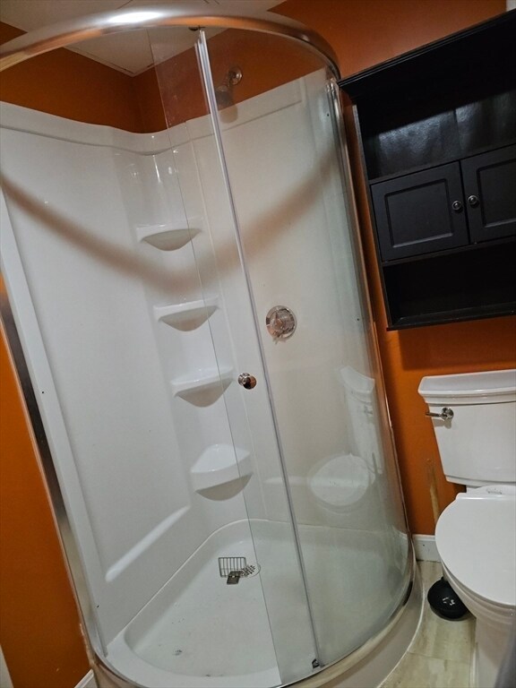 bathroom with tile patterned flooring, a shower with shower door, and toilet