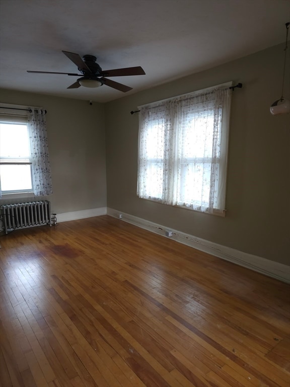 unfurnished room featuring hardwood / wood-style flooring, ceiling fan, and radiator heating unit