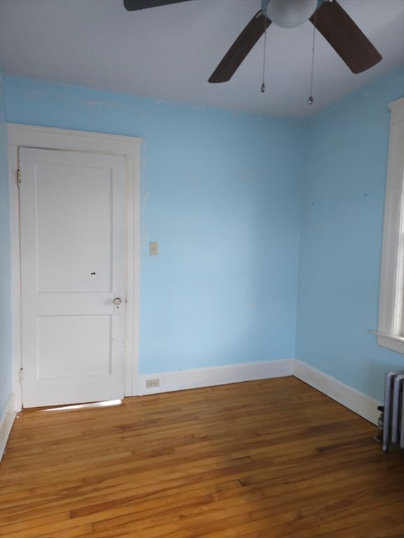 empty room with hardwood / wood-style floors, ceiling fan, and radiator heating unit