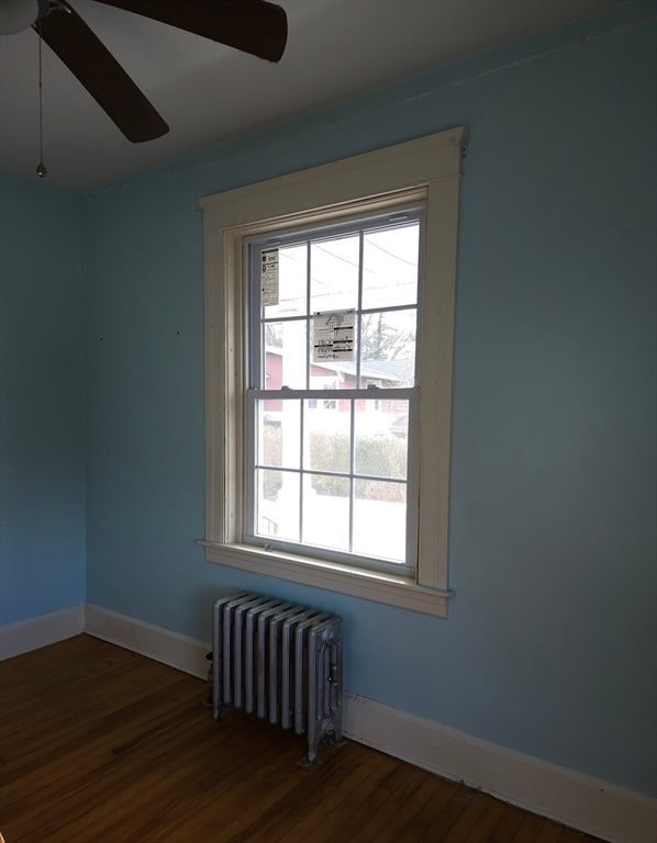 empty room featuring radiator heating unit, dark hardwood / wood-style flooring, and ceiling fan