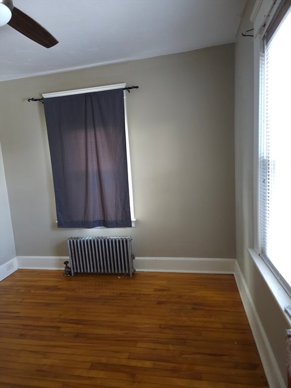 spare room with hardwood / wood-style flooring, ceiling fan, a healthy amount of sunlight, and radiator