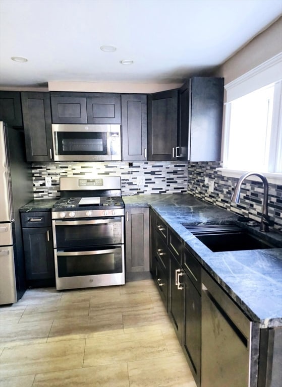 kitchen featuring backsplash, stainless steel appliances, dark stone counters, and sink