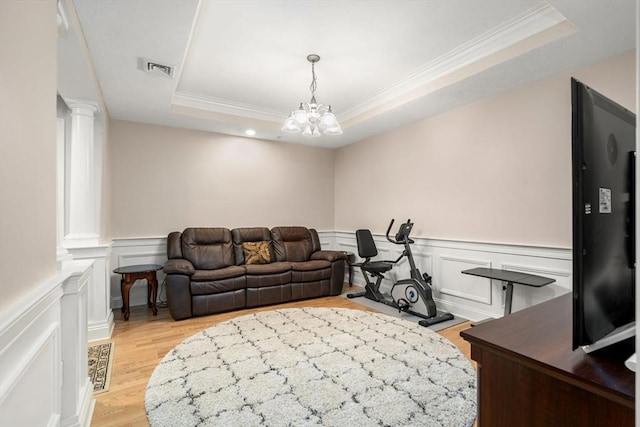 living room featuring light hardwood / wood-style floors, decorative columns, a tray ceiling, a chandelier, and crown molding