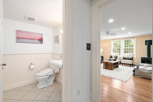bathroom featuring ceiling fan, visible vents, wainscoting, a wood stove, and baseboards