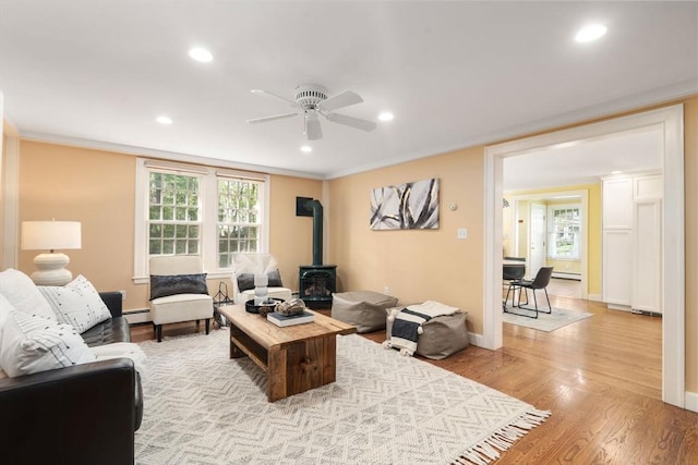 living room with a ceiling fan, a wood stove, light wood-type flooring, a baseboard heating unit, and recessed lighting