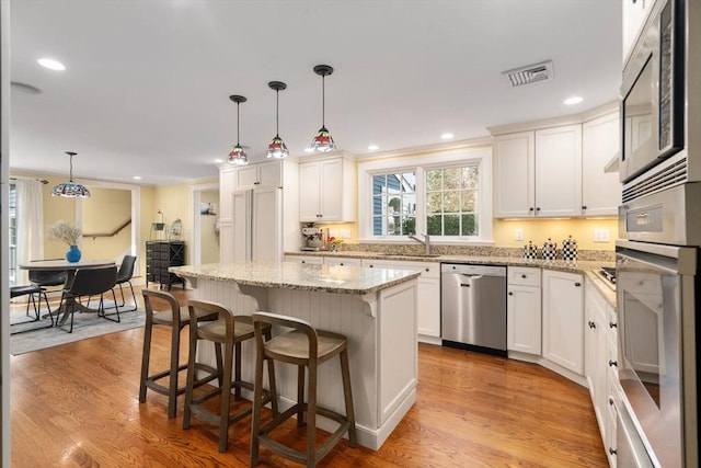 kitchen featuring a kitchen breakfast bar, pendant lighting, appliances with stainless steel finishes, a sink, and light wood-style flooring