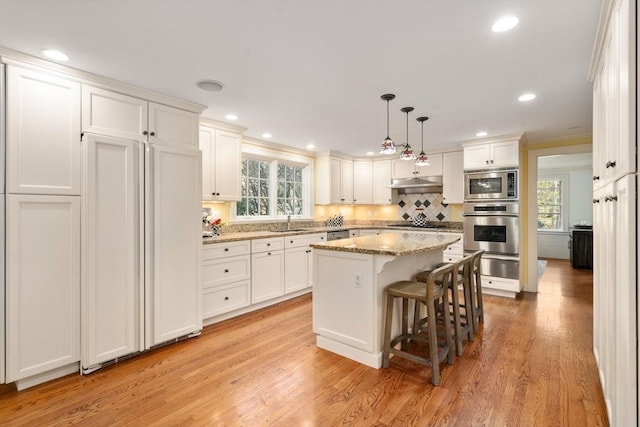 kitchen with a warming drawer, a sink, built in appliances, under cabinet range hood, and white cabinetry