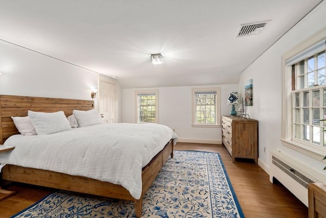 bedroom featuring radiator heating unit, baseboards, wood finished floors, and visible vents