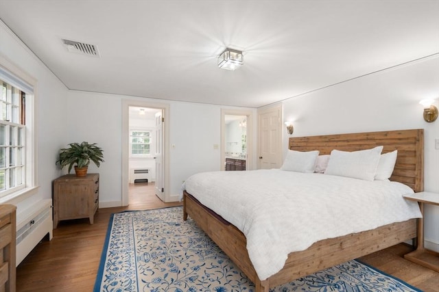 bedroom with visible vents, wood finished floors, baseboards, radiator heating unit, and ensuite bathroom