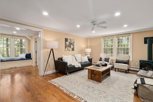 living area featuring a ceiling fan, baseboard heating, a wood stove, and recessed lighting