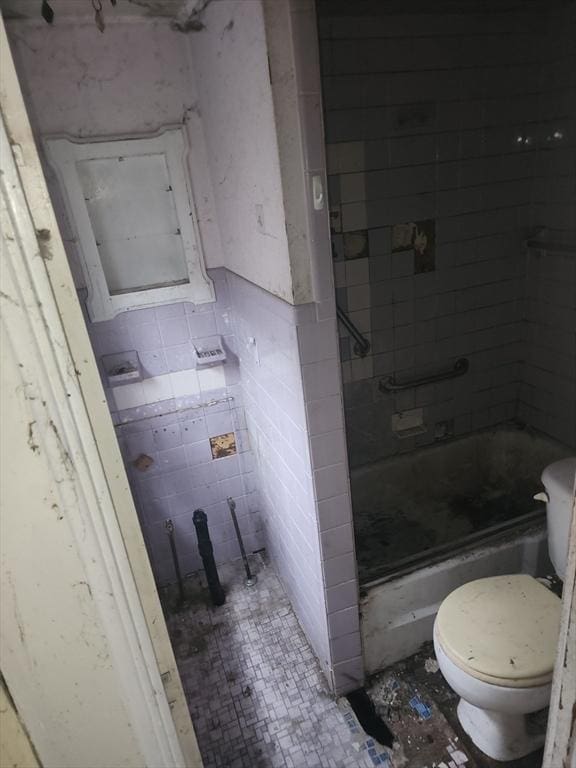 bathroom featuring toilet, tile walls, a shower, and a wainscoted wall