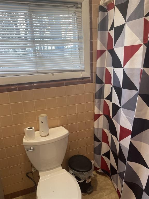 bathroom featuring toilet, tile walls, and a shower with curtain