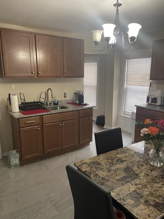 kitchen featuring a sink, dark stone counters, an inviting chandelier, and decorative light fixtures