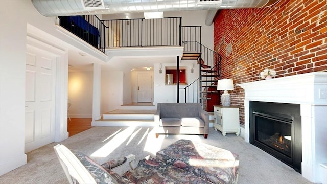 52 Sanborn St Unit 408, Reading, MA 01867 - carpeted living room featuring stairway, a towering ceiling, visible vents, a glass covered fireplace, and brick wall