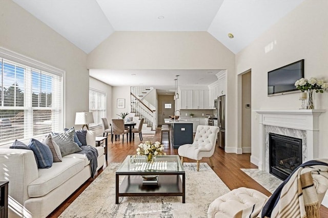 living room featuring vaulted ceiling, sink, a high end fireplace, and light hardwood / wood-style flooring