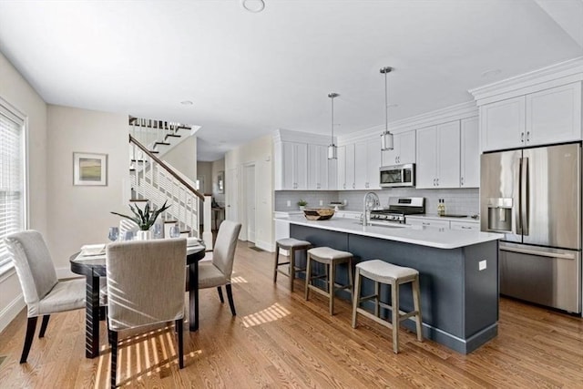 kitchen with a breakfast bar area, appliances with stainless steel finishes, an island with sink, pendant lighting, and white cabinets