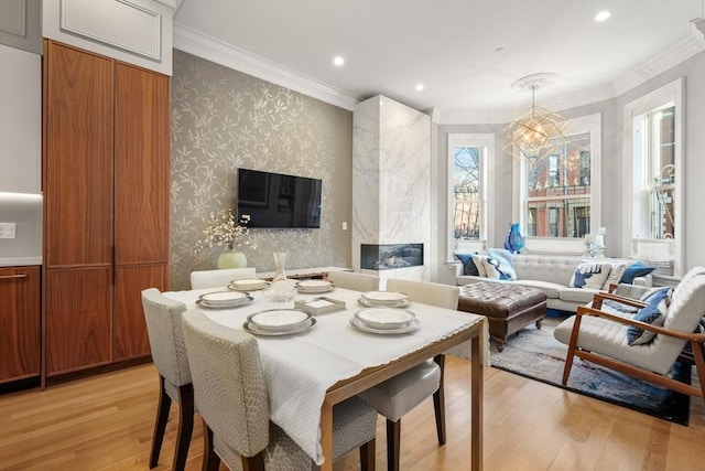 dining space with a fireplace, an inviting chandelier, ornamental molding, and light wood-type flooring