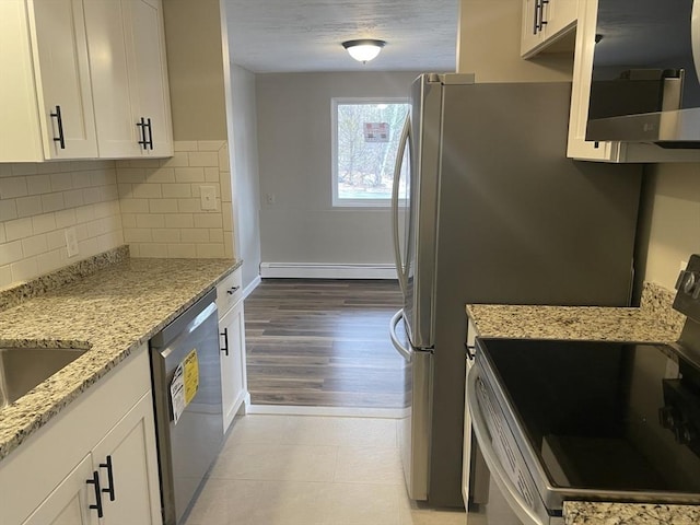 kitchen featuring white cabinets, a baseboard radiator, light stone countertops, stainless steel appliances, and backsplash