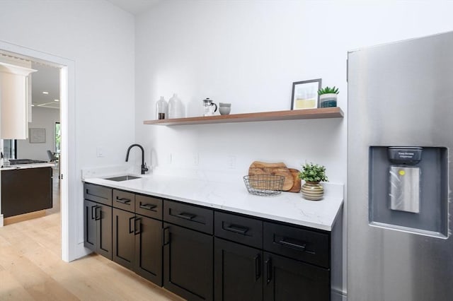 bar featuring sink, stainless steel fridge with ice dispenser, light stone counters, and light hardwood / wood-style flooring