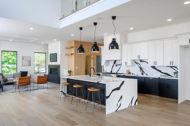 kitchen featuring a large island, decorative light fixtures, a breakfast bar, light wood-type flooring, and white cabinetry