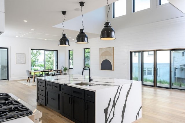 kitchen featuring an island with sink, light wood-type flooring, decorative light fixtures, a water view, and sink