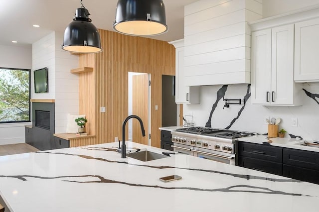 kitchen with double oven range, white cabinets, decorative light fixtures, a large fireplace, and sink