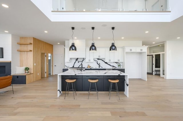 kitchen featuring a large island with sink, light stone countertops, white cabinets, a kitchen bar, and pendant lighting