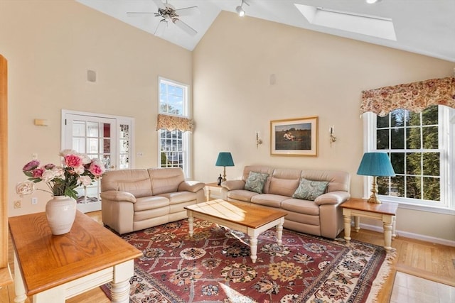 living area featuring wood finished floors, a ceiling fan, baseboards, high vaulted ceiling, and a skylight