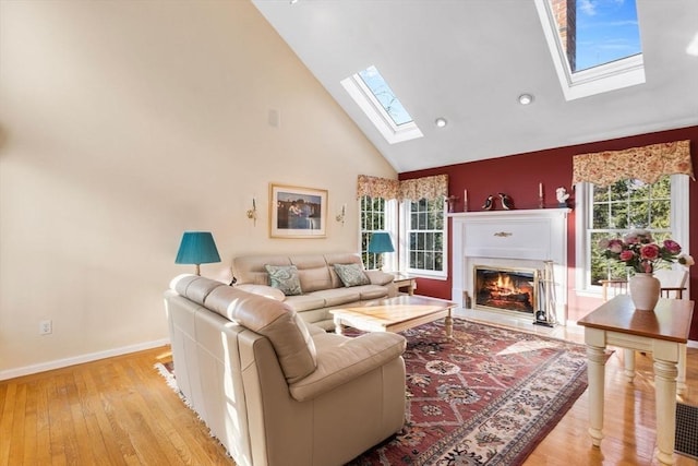 living room with a skylight, a healthy amount of sunlight, high vaulted ceiling, and light wood-style flooring