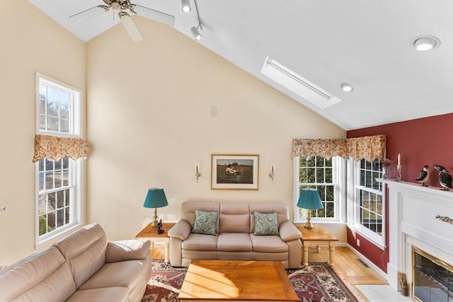 living area with a skylight, a fireplace, ceiling fan, track lighting, and light wood-style floors