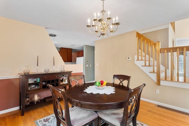 dining room featuring baseboards, visible vents, light wood finished floors, stairs, and a notable chandelier