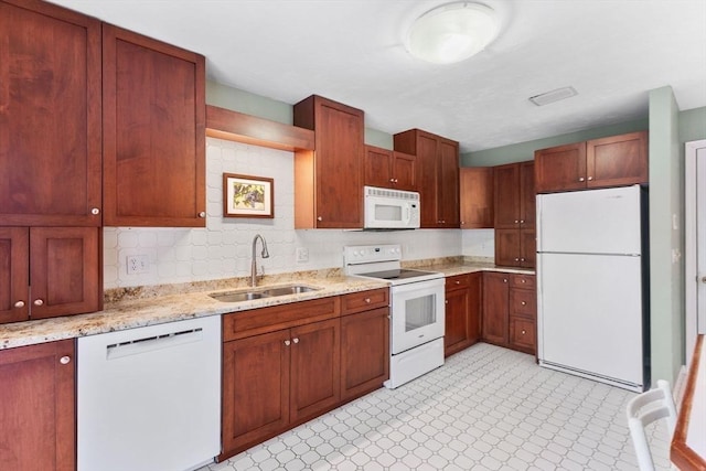 kitchen with a sink, white appliances, light floors, and light stone counters