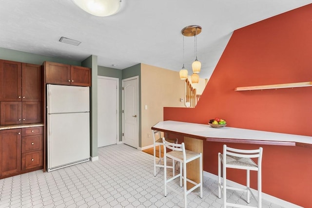 kitchen featuring a breakfast bar area, baseboards, freestanding refrigerator, and pendant lighting