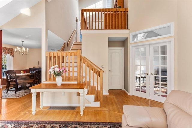 stairway with a chandelier, a high ceiling, wood finished floors, and french doors