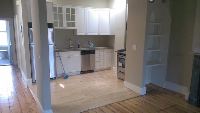 kitchen with a sink, stainless steel appliances, glass insert cabinets, white cabinetry, and light wood-type flooring
