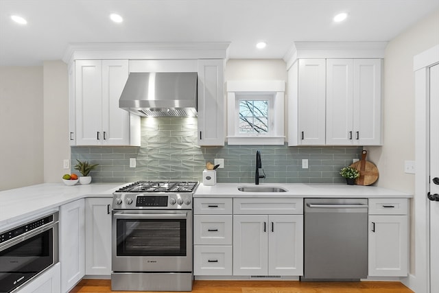 kitchen featuring wall chimney exhaust hood, white cabinetry, sink, and appliances with stainless steel finishes