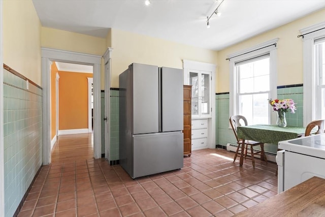 kitchen with freestanding refrigerator, wainscoting, tile walls, a baseboard heating unit, and tile patterned floors