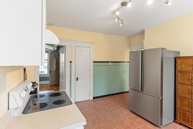 kitchen featuring freestanding refrigerator, wainscoting, tile walls, white electric range, and light countertops