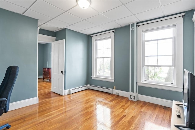 unfurnished office with light wood-type flooring, baseboards, a drop ceiling, and a healthy amount of sunlight