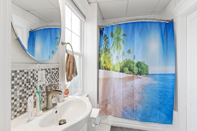 full bathroom featuring curtained shower, a drop ceiling, decorative backsplash, and a sink